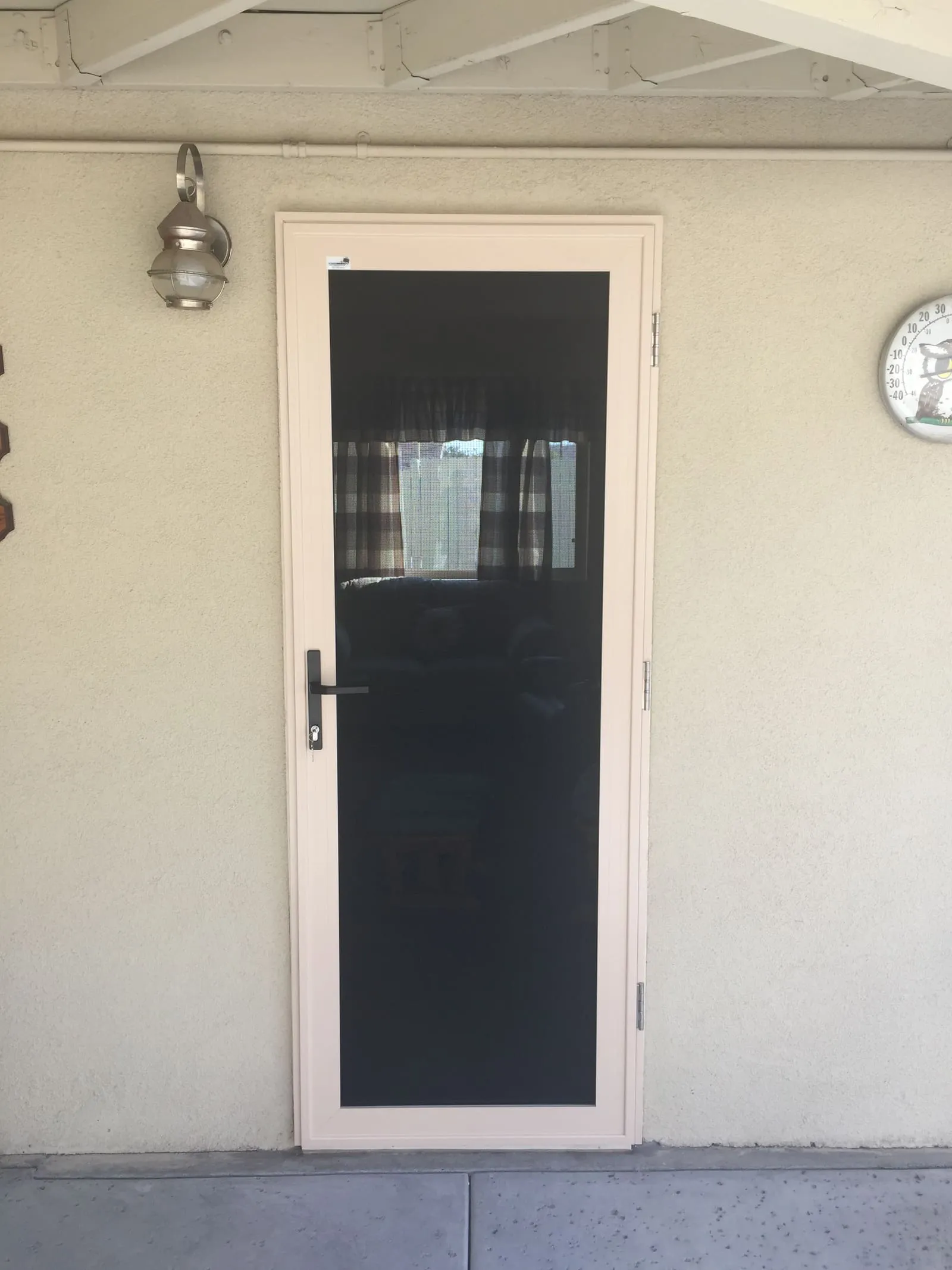 Almond hinged security screen door on a cream stucco entry, plaid curtain visible through the mesh
