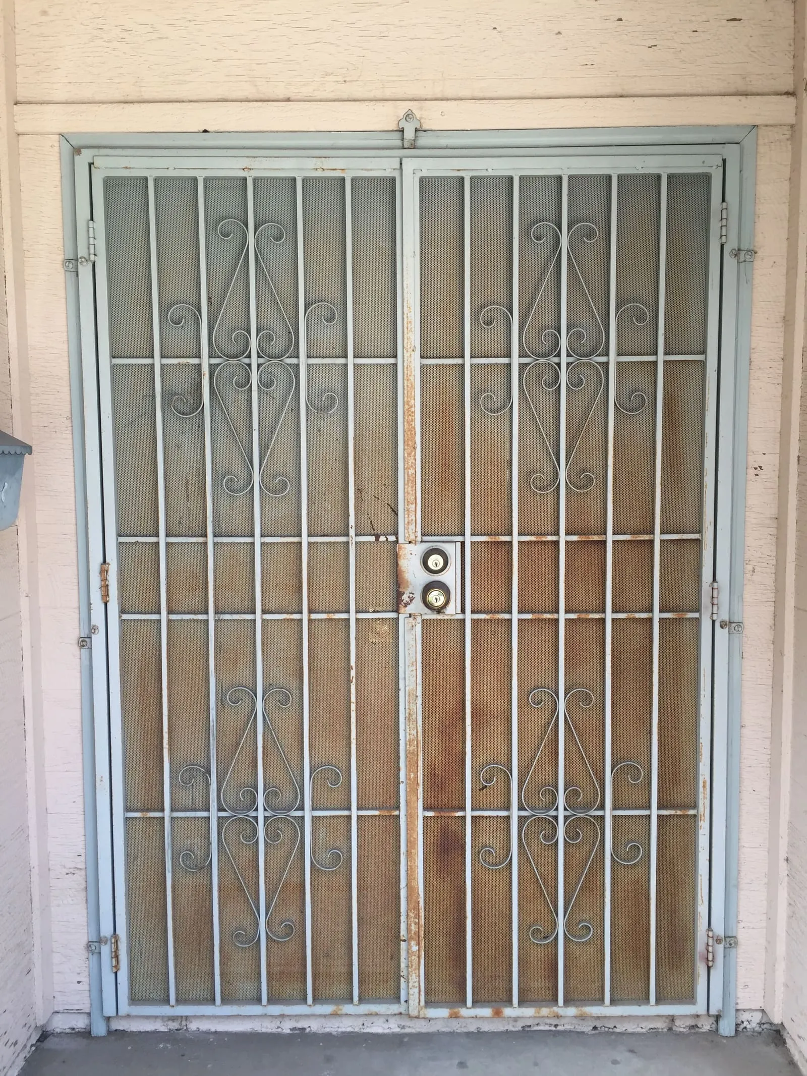 An old scroll-front double security screen door, rusted through at the hinges and lock rail