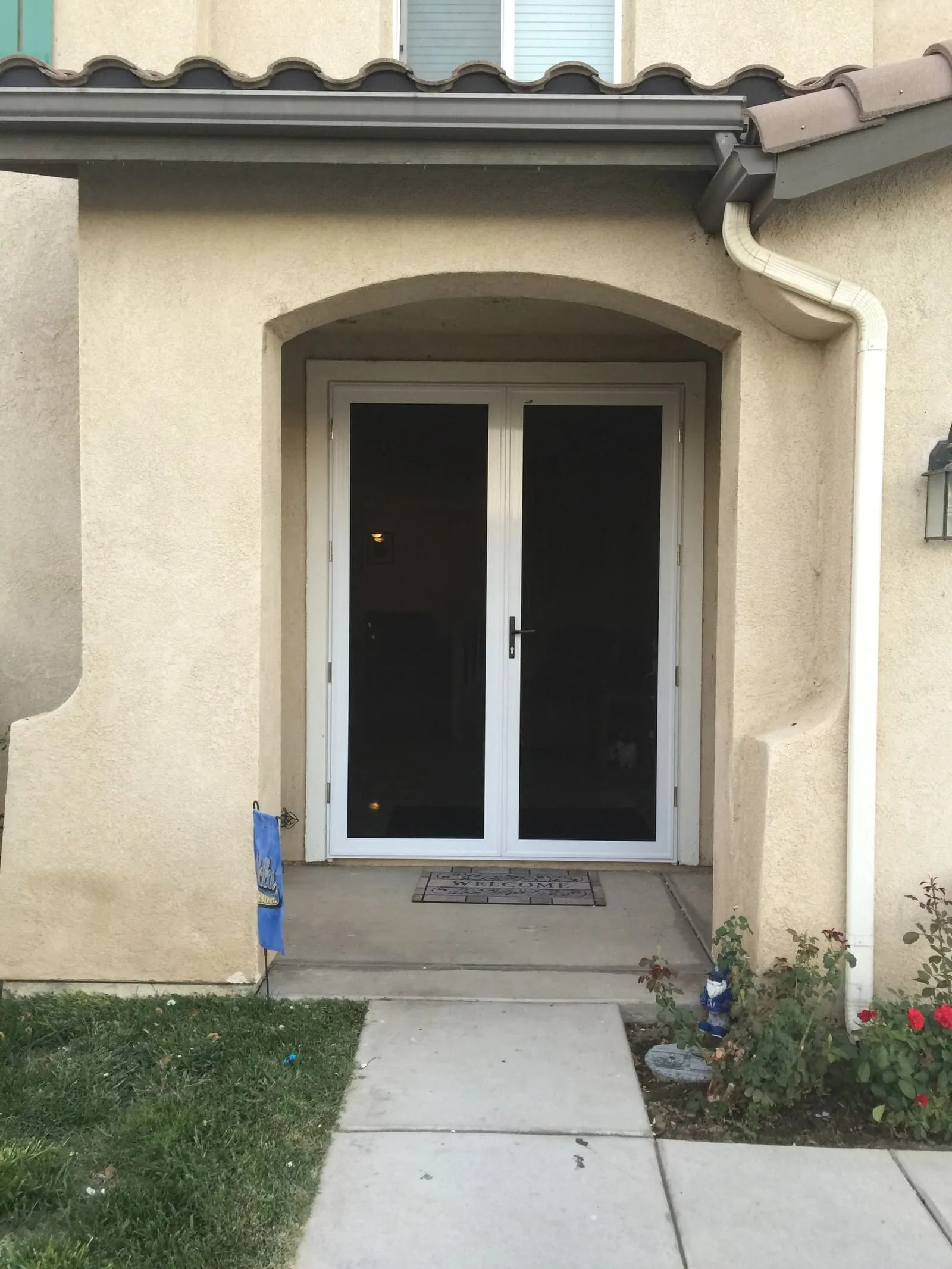 White French-pair security screens under an arched stucco entry with a welcome tile