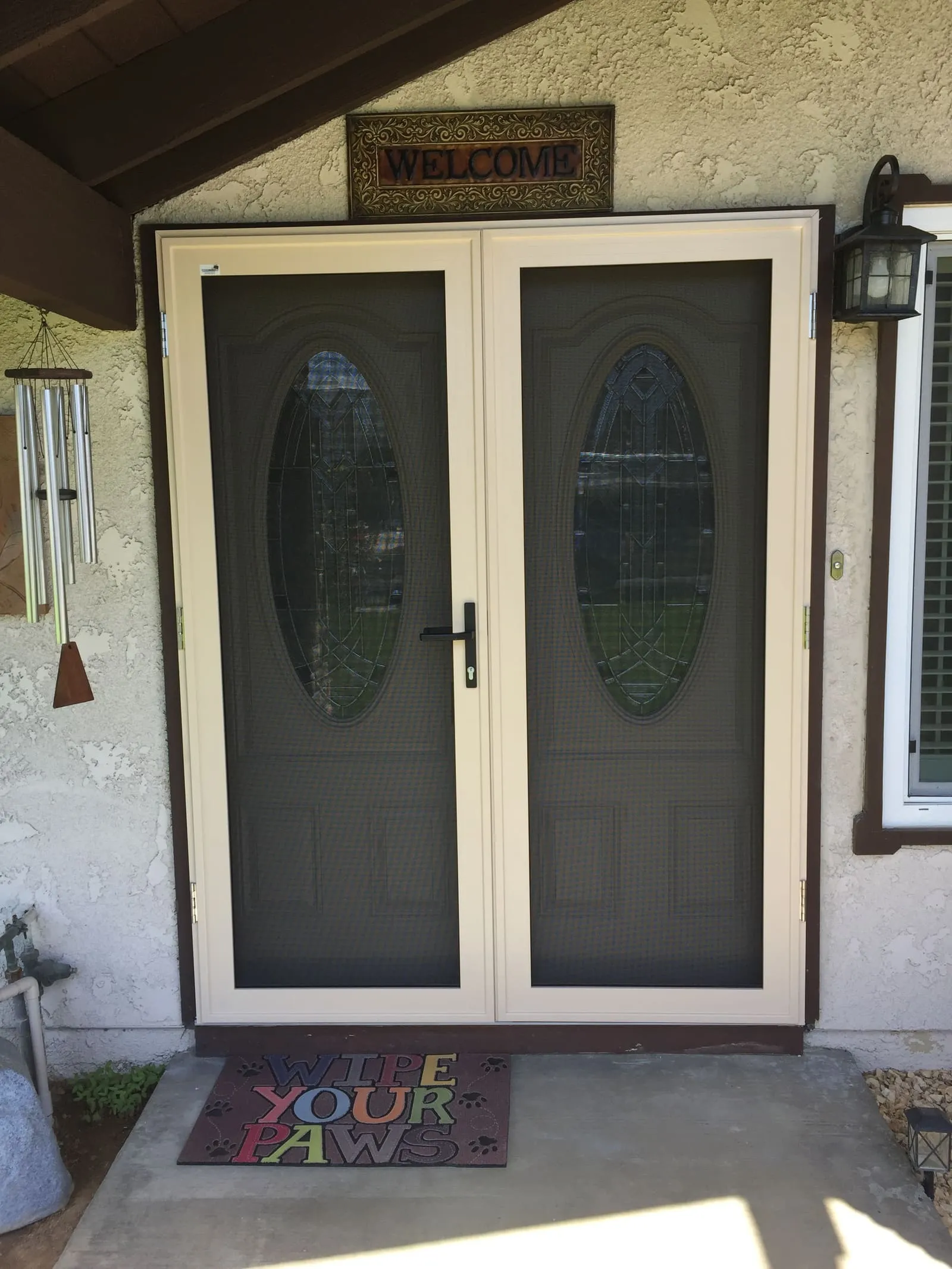 Almond French-pair security screens on a brown-trim entry, oval glass doors visible behind the mesh