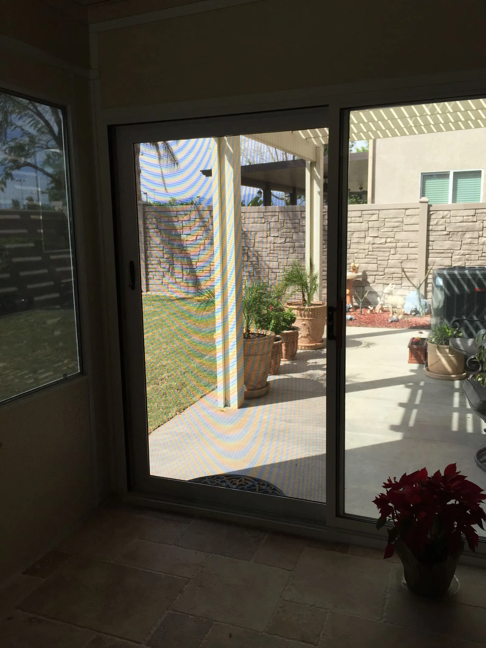 View from inside through a sliding security screen to a patio, with visible rainbow moire from the camera