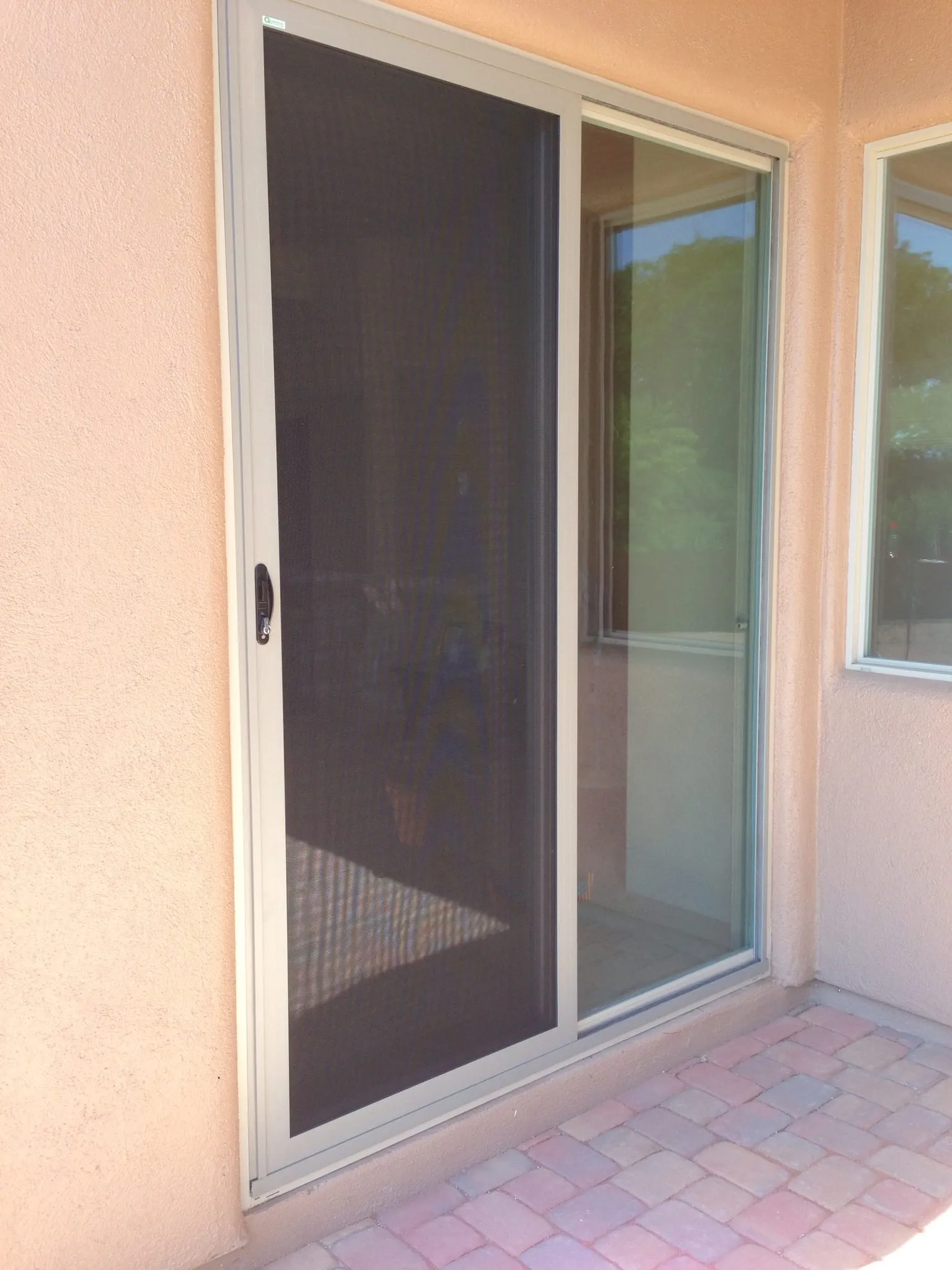 A tan-framed Daylight Steel sliding security door beside the open glass slider it protects