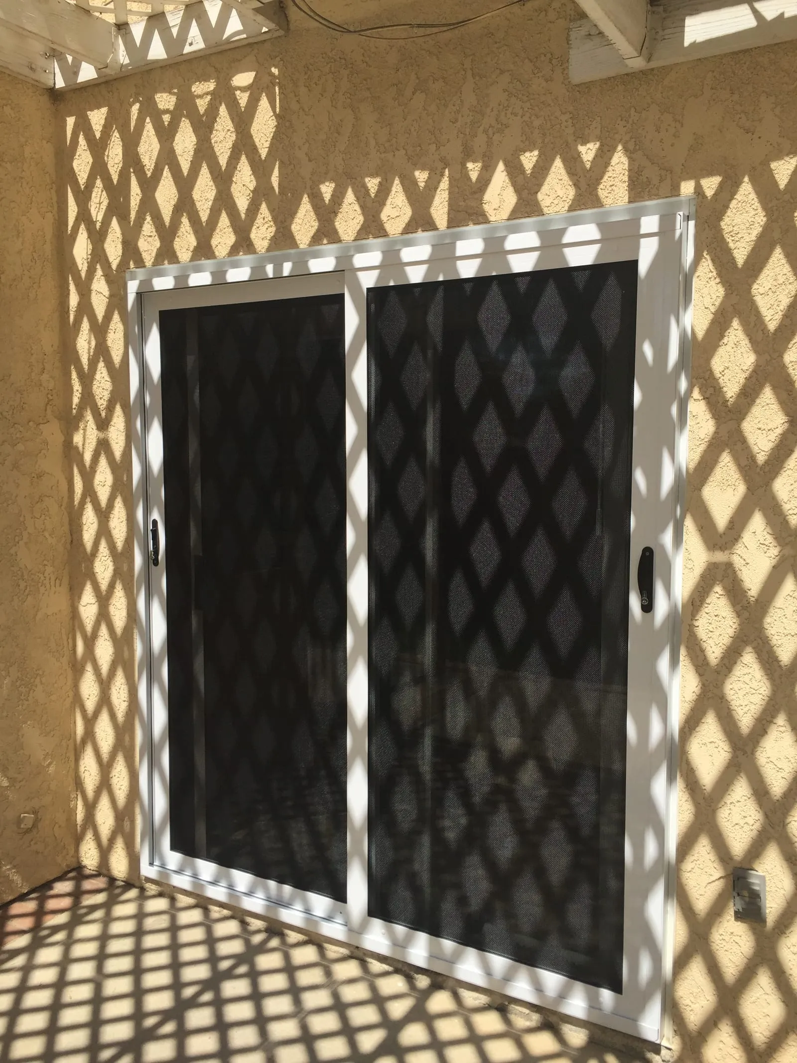 White-framed security window screen under afternoon lattice shadows