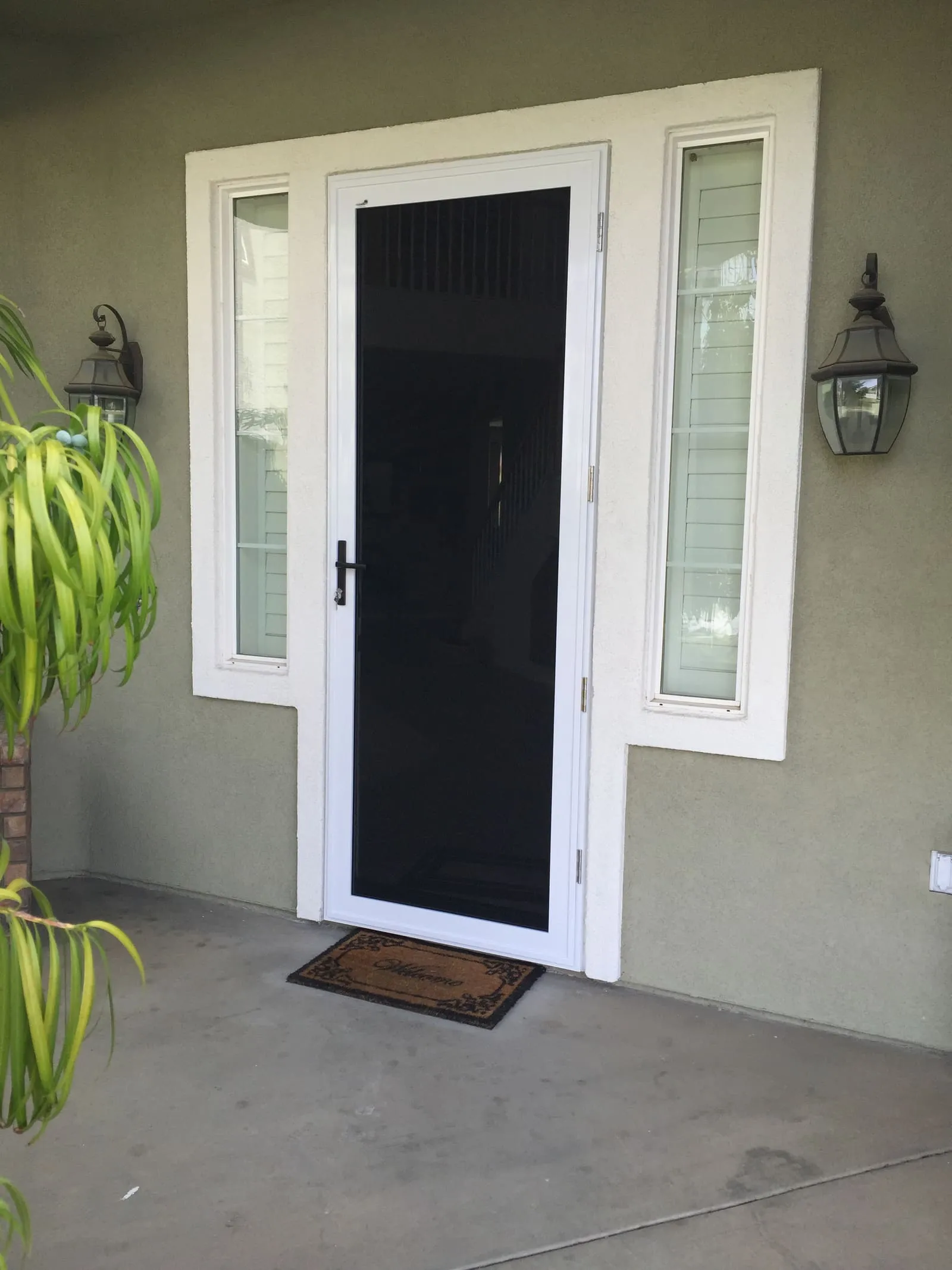 White full-view hinged security screen door between two sidelite windows on a green stucco wall